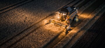 A combine harvester is illuminated at night as it harvests a field of crops, showcasing heavy machinery in action.