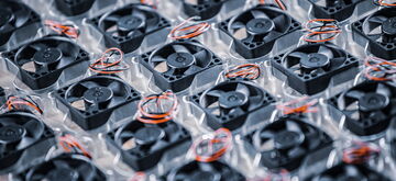 Rows of black computer cooling fans with red wires are neatly arranged on a transparent plastic tray.