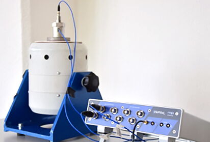 A compact measurement system setup with a white cylindrical device and a blue control unit connected by cables.