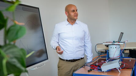 A man in a white shirt stands next to a display and equipment, presenting a training session.
