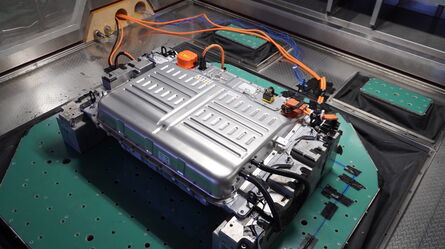 An electric vehicle battery pack is displayed on a testing platform with various cables connected for analysis.