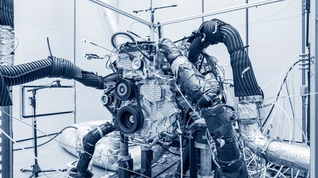 A complex engine setup with various tubes and wires is displayed in a mechanical testing facility.