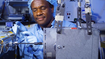 A technician in a blue lab coat and hairnet carefully adjusts equipment in a high-tech laboratory setting.