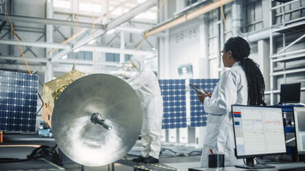 Scientists in a lab conduct force-limited vibration testing on a satellite with solar panels using advanced equipment.
