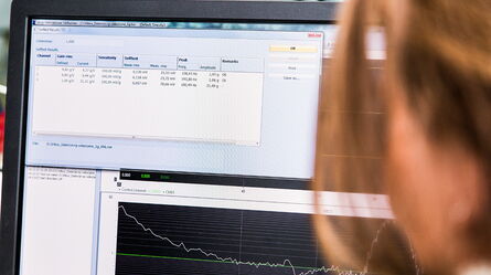 A person analyzes data on a computer screen displaying graphs and compliance metrics in an office setting.