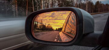 A vibrant sunset reflects in a car's side mirror on an open road, capturing a scenic automotive journey.