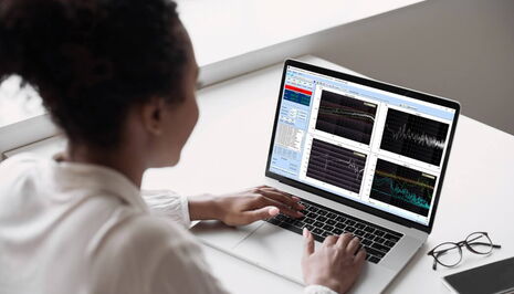 A person analyzes vibration control data on a laptop screen displaying multiple graphs in a bright office setting.