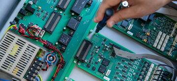 A hand uses a screwdriver to repair a circuit board in a hardware maintenance setup.
