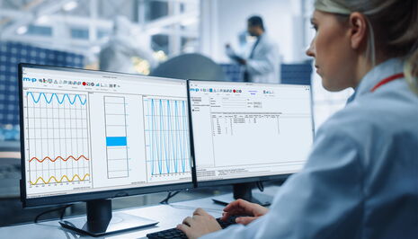 A scientist analyzes strain data on dual monitors in a modern laboratory setting.