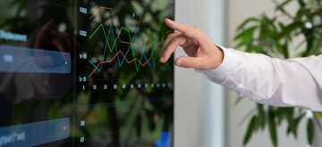 A person interacts with a touchscreen displaying colorful software demo graphs and charts in an office setting.