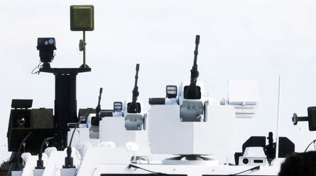 A row of advanced military vehicle turrets equipped with weaponry and surveillance systems is displayed under a clear sky.