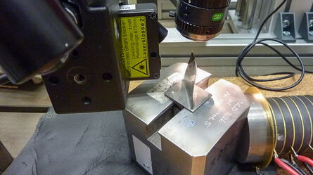 A precision laser machine works on a metal block in an industrial setting, showcasing advanced manufacturing technology.