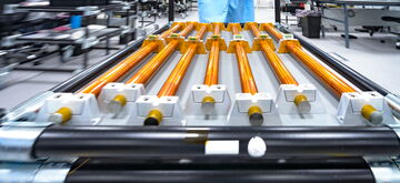 A technician in protective gear handles a complex assembly of orange rods in a high-tech laboratory setting.