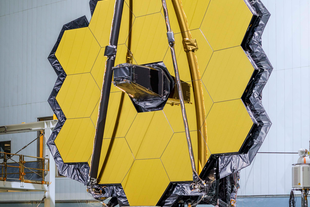 The image shows the large, intricately designed hexagonal mirror of a space telescope inside a laboratory.