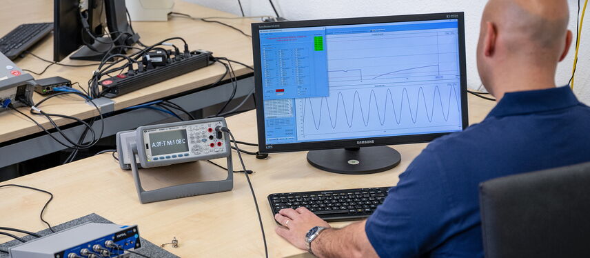 A technician analyzes data on a computer screen for calibration in an electronics lab.