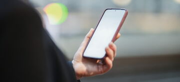 A person holds a mobile phone, set against a blurred urban background.