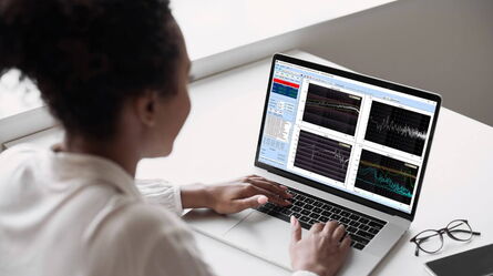 A person analyzes vibration control data on a laptop screen displaying multiple graphs in a bright office setting.