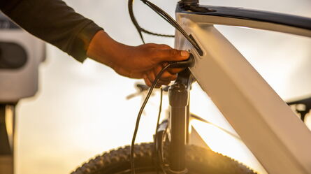 A person charges an electric bicycle, highlighting support for emerging electromobility technologies at sunset.