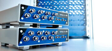 Two VibPilot devices with multiple connectors are stacked in front of a blurred VibRunner setup.