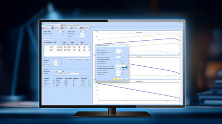 A computer monitor displays data analysis software with graphs of acceleration, velocity, and displacement in a dimly lit room.