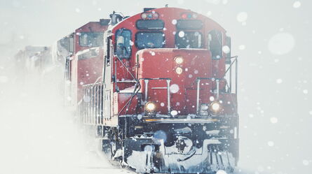 A red train powers through a snowy landscape, highlighting integrated environmental challenges.