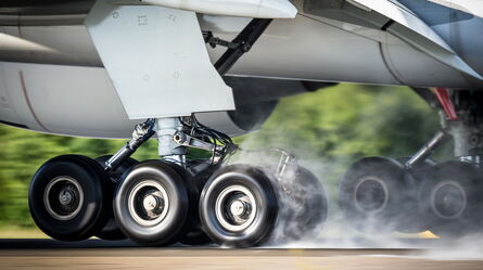 An airplane's landing gear touches down on the runway, with smoke rising as wheels absorb the shock of realistic aviation loads.