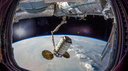 A spacecraft arm deploys a cylindrical module above Earth, viewed from a space station window during structural analysis.